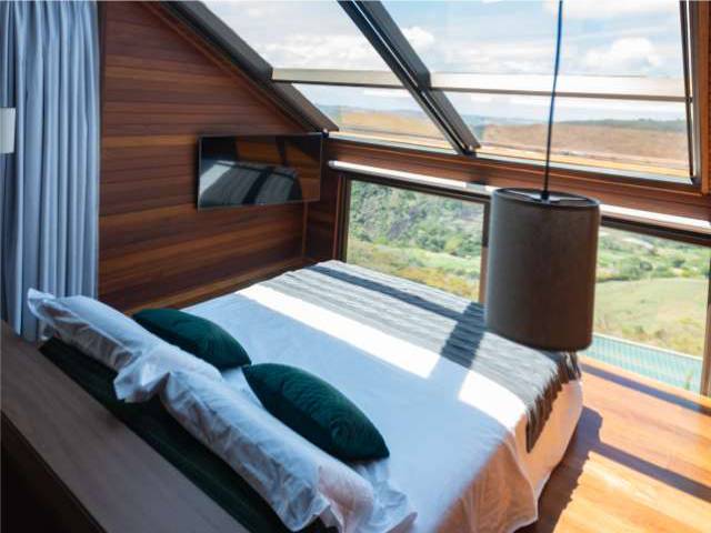Cama sob a claraboia da cabana, com almofadas verdes e a vista das montanhas ao amanhecer