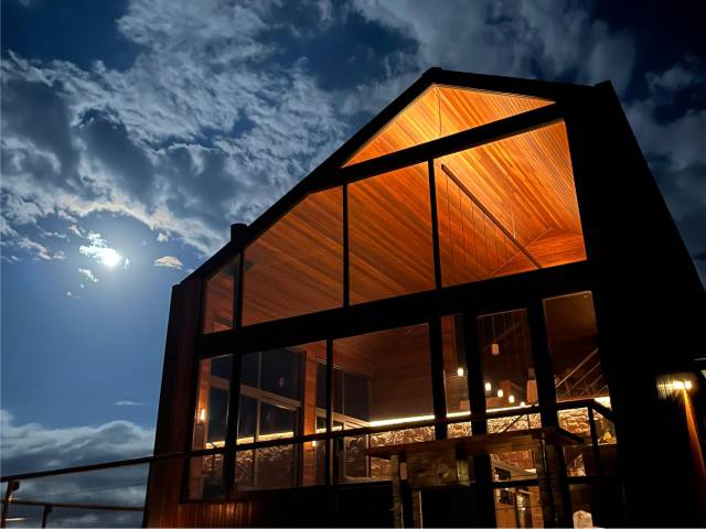 Fachada de vidro da cabana iluminada à noite, sob o luar e as nuvens