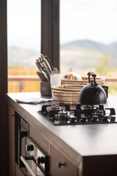 Detalhe da cozinha da cabana com utensílios e a paisagem montanhosa pela janela
