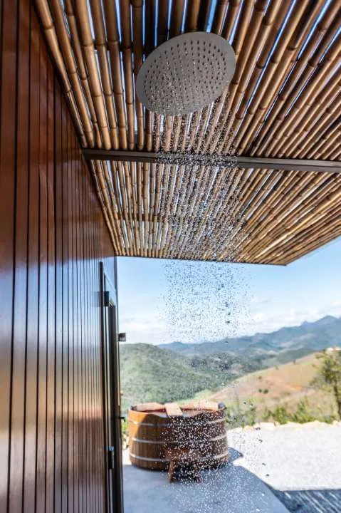 Ducha ao ar livre sob teto de bambu, com o ofurô e o vale ao fundo